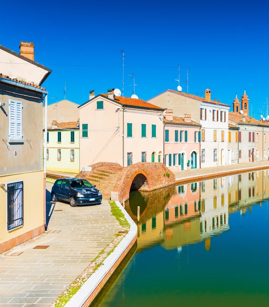 A street of the small Italian town of Comacchio. Colored houses reflected in water. Stone bridge and water canal in venetian style.