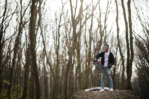 Street style arab man in eyeglasses with longboard on wood