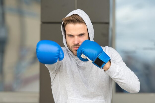 Strength and motivation. Sportsman concentrated training boxing gloves. Athlete concentrated face with sport gloves practice fighting skills urban background. Boxer handsome strict coach practicing.