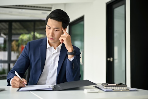 Stressed Asian businessman examining financial reports working at his desk