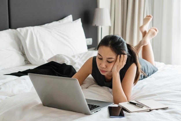 Stressed Asian businesswoman working on laptop computer in bed at hotel Business trip people and technology concept copy space