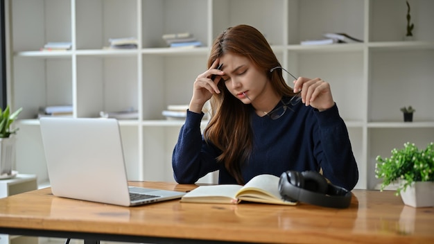 A stressed Asian woman suffers from headaches and eye strain during work at her desk