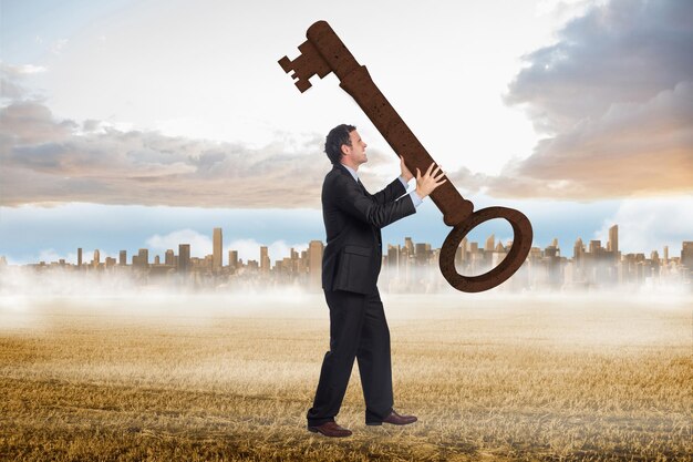 Photo stressed businessman carrying large key against large city on the horizon past yellow field