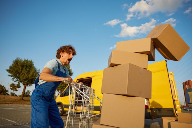 Stressed clumsy courier screaming looking at falling parcel boxes from fully loaded trolley cart Accident at work