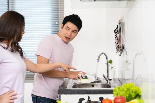 Stressed couple conflict in their kitchen angry woman pointing hand to man for washing dishes