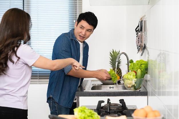 Stressed couple conflict in their kitchen angry woman pointing hand to man for washing vegetables