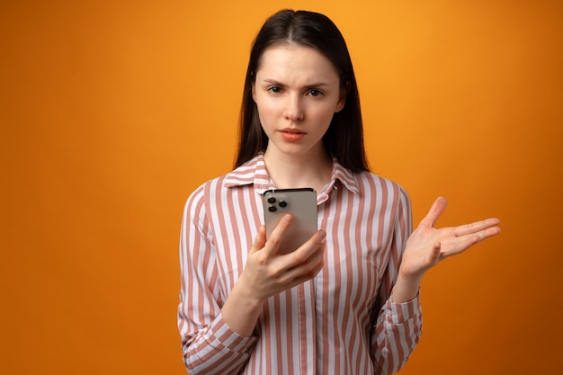 Stressed frustrated young woman holding smartphone recieved bad news yellow background