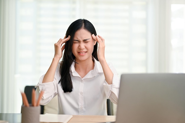 Stressed and furious Asian businesswoman sitting at desk in the office