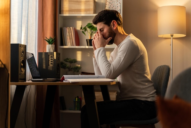 Stressed male entrepreneur having problems at work. Depressed caucasian man sitting upset at desk with laptop at home and touching head in despair