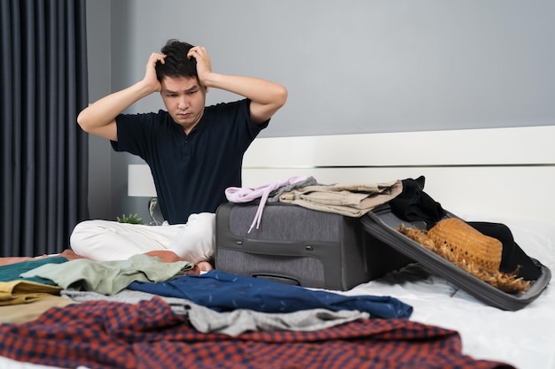 Stressed man having problem with packing clothes into suitcase on bed holiday travel concept