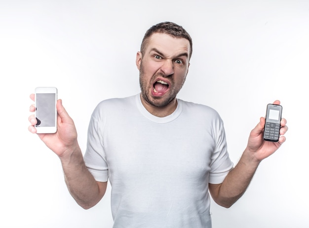 Stressed man is holding two different phones made in different years. Technologies are changing so fast that this changes are stressful to him. Isolated on white background