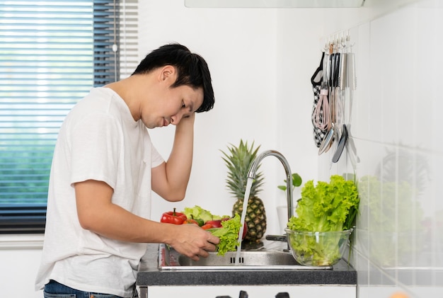 Stressed man washing vegetables in the sink in the kitchen at home