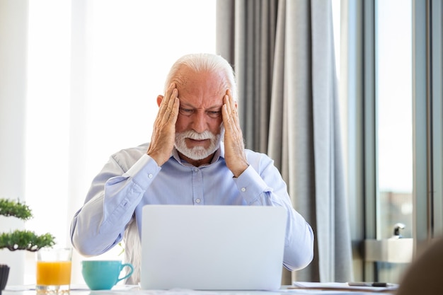 Stressed mature businessman with laptop He could also have a headache He is sitting in the boardroom There are documents and laptop on the table Copy space