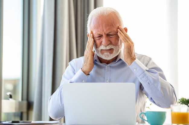 Stressed mature businessman with laptop He could also have a headache He is sitting in the boardroom There are documents and laptop on the table Copy space