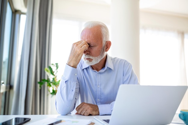 Stressed mature businessman with laptop He could also have a headache He is sitting in the boardroom There are documents and laptop on the table Copy space