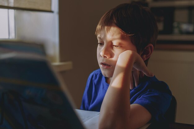 stressed tired boy doing homework at home at the desk by the window