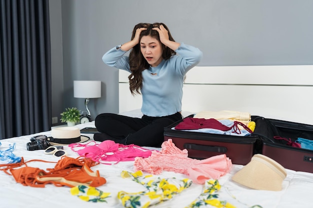 Stressed woman having problem with packing clothes into suitcase on a bed at home holiday travel concept