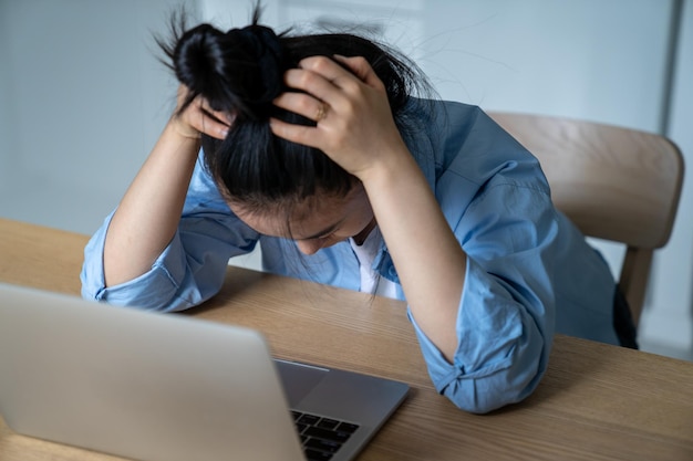 Stressed woman sitting at desk with laptop holding head in hands having online business problems