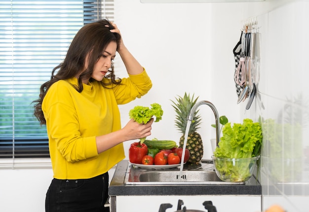 Stressed woman washing vegetables in the sink in the kitchen at home