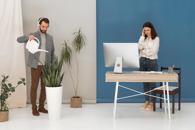 Stressed woman working on computer and man is watering plant