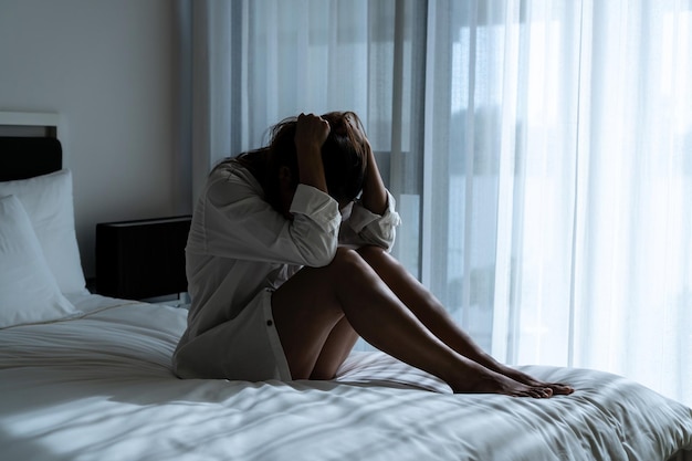 Stressed young Asian woman suffering on depression and sitting alone in dark bedroom at home Sad unhappy disappointed domestic abuse or stop violence and rape concept