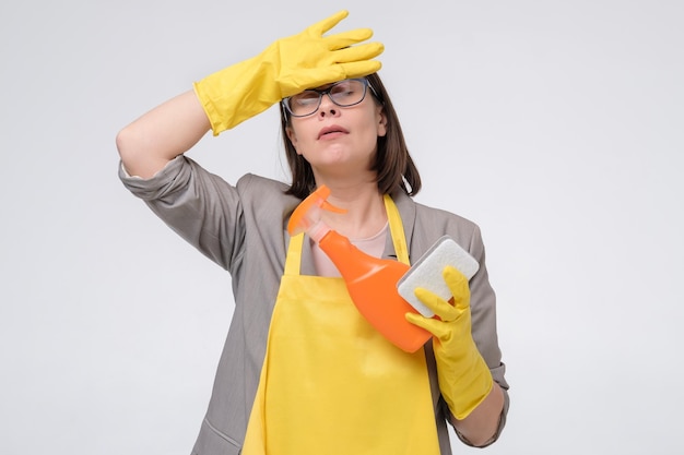 Stressed young housewife in a yellow apron with kitchen spongeand a bottle of detergent