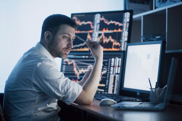 Stressful day at the office. Young businessman holding hands on his face while sitting at the desk in creative office. Stock Exchange Trading Forex Finance Graphic 