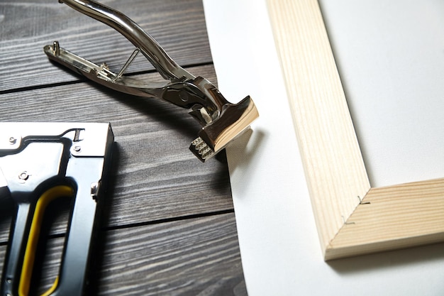 Stretching canvas on wooden stretcher bar staple gun and canvas pliers on a brown table