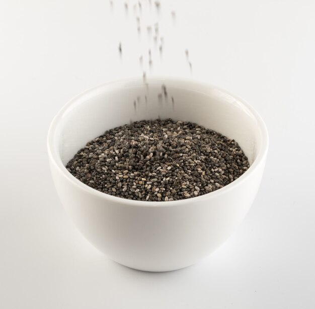 Strewing Chia Seeds in White Bowl on Light Background. Salvia Hispanica also Known as Superfood