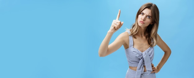 Strict seriouslooking young mother giving directions raising index finger and frowning to look scary