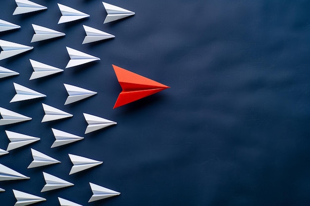 A striking red paper plane leading a formation of white ones against a blue backdrop symbolizing le