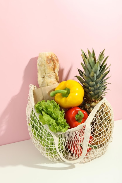 String bag with grocery on white table against pink background