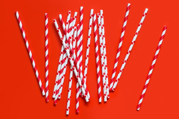 Striped and dotted paper drinking straws on red background top view