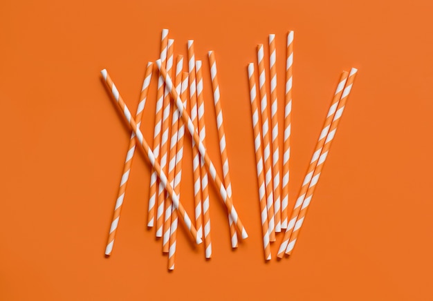 Striped paper drinking straws on orange background top view. Eco friendly and biodegradable