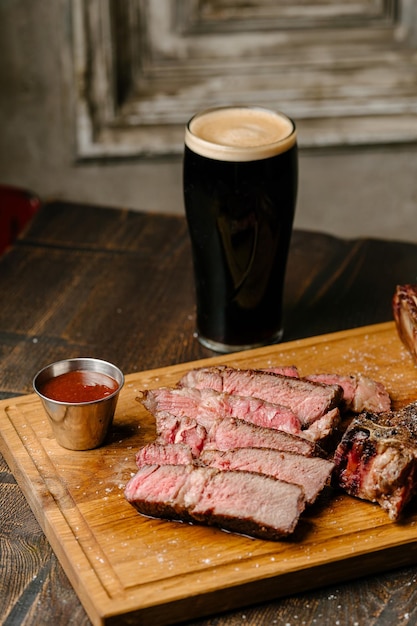 Striploin steak from marbled beef New york steak on a wooden board with a glass of dark beer and barbecue sauce