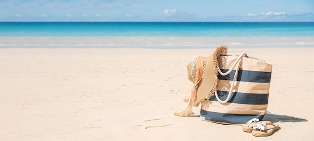 Stripy navy blue beach bag, straw hat and flip flops on tropical beach at sunny day