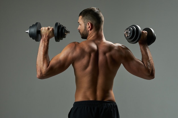 Strong athlete man in black sportswear posing at the photo camera in room indoors