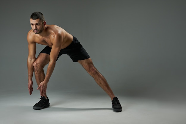 Strong athlete man with powerful torso warming up isolated on grey background