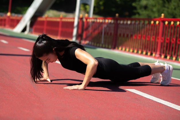 Strong athlete woman doing plank exercise outdoor at the bridge in sunny morning