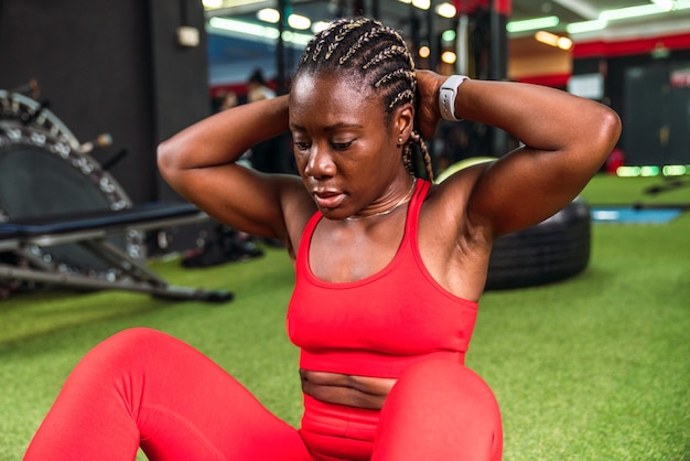 Strong athletic black woman in a gym doing abdominal exercises in red sportswear