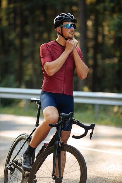 Strong bearded man in sport outfit and eyeglasses adjusting protective helmet before morning ride on fresh air