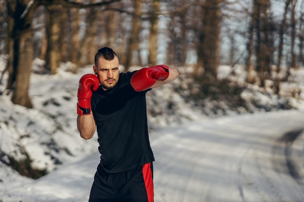 Strong boxer with boxing gloves standing in nature at snowy winter day and sparring. Boxing in nature, healthy life, winter sport