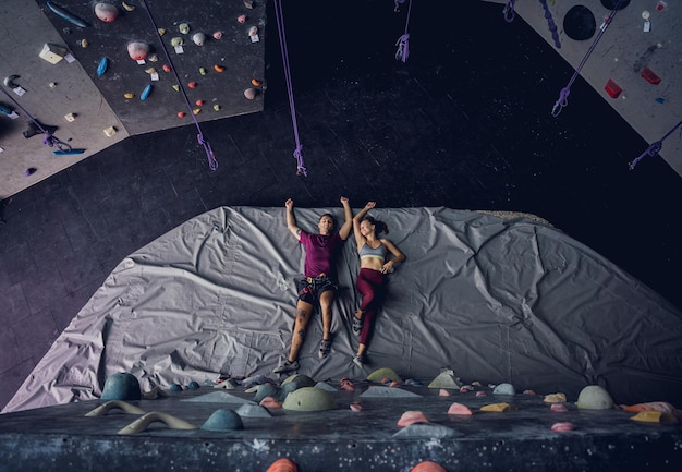 Photo a strong couple of climbers relax near artificial wall with colorful grips and ropes