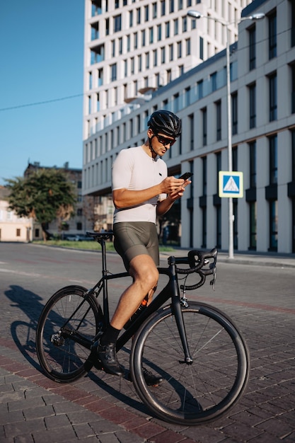 Strong cyclist in safety helmet ad mirrored glasses texting on smartphone while standing outdoors with his bike Relaxation after workout Gadgets for lifestyles