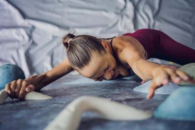 A strong female climber climbs an artificial wall with colorful grips and ropes