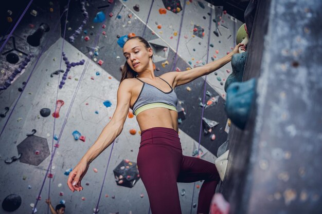 A strong female climber climbs an artificial wall with colorful grips and ropes