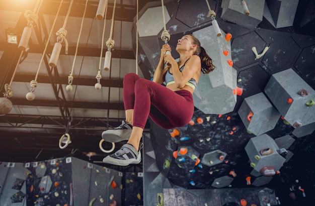 A strong female climber climbs an artificial wall with colorful grips and ropes