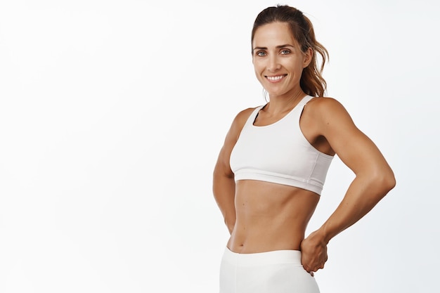 Strong and fit fitness woman 40 years old abs and muscles smiling and looking confident after workout white background