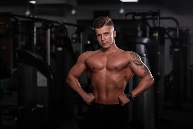 Strong handsome fitness model man with a sports body and tattoo on hand does a workout in the gym