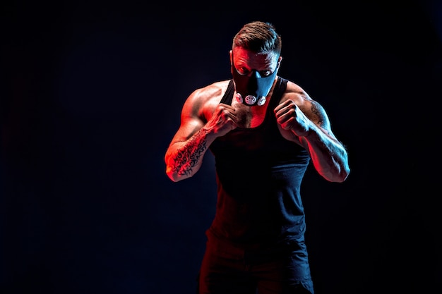 Strong male athlete in a black training mask on a black wall